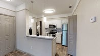 This single-story residence is designed with a neutral, cohesive color palette throughout, creating a clean and functional living environment. The kitchen serves as a central highlight, featuring white cabinetry, light stone-look countertops, and a full suite of stainless steel appliances including an electric range, over-the-range microwave, dishwasher, and refrigerator. A peninsula with an extended countertop defines the boundary between the kitchen and adjoining living areas, complemented by pendant lighting overhead. Wood-look flooring runs through the kitchen and extends into connecting areas, adding warmth and durability.

The living room is generously sized, finished with plush carpeting, a ceiling fan with integrated lighting, and a sliding glass door that introduces natural light and outdoor access. A secondary entry area provides additional space near the front door, also finished with carpet.

The bedrooms are carpeted and each equipped with ceiling fans, windows for natural light, and closets with built-in hanging storage. The primary bathroom features a wide vanity with stone-look countertops and white cabinetry, while the second bathroom includes a full tub-shower combination with wood-look tile flooring throughout both.