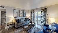 This single-floor residence offers a thoughtfully designed layout that balances functionality with contemporary style. The living room serves as the heart of the home, featuring wood-look flooring, neutral gray walls, and a trio of framed wall art above a comfortable sofa. A sliding glass door floods the space with natural light and provides direct access to a private outdoor patio, creating a seamless indoor-outdoor connection.

The galley-style kitchen is equipped with dark espresso cabinetry, white quartz countertops, and a full suite of stainless steel appliances, including a refrigerator, electric range, microwave, and dishwasher. An adjacent dining area with bar seating offers a convenient space for casual meals.

The primary bedroom features plush carpeting, warm ambient lighting, and a walk-in closet, providing ample storage. A second bedroom is equally well-appointed with carpeted flooring, large windows with decorative draping, and generous natural light. The residence includes two bathrooms: one featuring a white vanity with an undermount sink and backlit mirror, and the other a clean, full bath with a tub-shower combination. Wood-look flooring extends throughout the common areas, tying the cohesive design together.