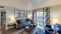 This single-floor residence offers a thoughtfully designed layout that balances functionality with contemporary style. The living room serves as the heart of the home, featuring wood-look flooring, neutral gray walls, and a trio of framed wall art above a comfortable sofa. A sliding glass door floods the space with natural light and provides direct access to a private outdoor patio, creating a seamless indoor-outdoor connection.

The galley-style kitchen is equipped with dark espresso cabinetry, white quartz countertops, and a full suite of stainless steel appliances, including a refrigerator, electric range, microwave, and dishwasher. An adjacent dining area with bar seating offers a convenient space for casual meals.

The primary bedroom features plush carpeting, warm ambient lighting, and a walk-in closet, providing ample storage. A second bedroom is equally well-appointed with carpeted flooring, large windows with decorative draping, and generous natural light. The residence includes two bathrooms: one featuring a white vanity with an undermount sink and backlit mirror, and the other a clean, full bath with a tub-shower combination. Wood-look flooring extends throughout the common areas, tying the cohesive design together.