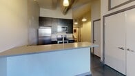 Located at 631 Campbell Ave SW in Roanoke, Virginia, this one-bedroom, one-bathroom loft offers an urban industrial aesthetic with thoughtfully designed living spaces. The unit's character is immediately established through its exposed painted brick walls, polished concrete floors, and elevated ceilings with visible ductwork — hallmarks of a converted industrial building.

The kitchen is a functional highlight, featuring stainless steel appliances including a refrigerator, electric range, and over-the-range microwave. Dark, wood-toned cabinetry provides ample storage and contrast against the light countertops. A peninsula-style breakfast bar separates the kitchen from the living area, offering additional prep space and casual seating. Pendant lighting above adds a warm, contemporary touch.

The bedroom is an intimate, well-defined space accessed through a striking shoji-style sliding panel door with a black grid frame, blending modern design sensibility with privacy. Polished concrete floors and tall ceilings continue throughout.

The bathroom is clean and efficiently laid out, featuring a full tub-shower combination with a sculpted surround, a dark wood wall cabinet for storage, and tile flooring. A connecting hallway ties all rooms together cohesively. This loft is ideal for those seeking an industrially styled, low-maintenance urban living space in downtown Roanoke.