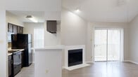 Located at 3719 William Dehaes Dr in Irving, Texas, this two-story home offers a thoughtfully designed layout spread across two levels. The main living area immediately draws attention with its vaulted ceilings that rise dramatically, amplifying the sense of openness throughout the space. A white-framed fireplace serves as a central focal point in the living room, complemented by light wood-tone flooring that extends throughout the main level.

The kitchen is integrated into the open-concept layout via a pass-through counter with a light stone-speckled surface, offering views into the living area. Dark cabinetry, a tile backsplash, and black appliances give the kitchen a defined, contrasting character. Natural light filters in through blinded windows, enhancing the airy feel of the main floor. A sliding glass door provides access to an outdoor area.

Upstairs, the carpeted bedrooms offer a quieter retreat. One bedroom features direct access to a spacious walk-in closet equipped with dual wire shelving systems. A full bathroom on this level includes a tub-shower combination, a vanity with stone-look countertops, and dark cabinetry consistent with the kitchen's design. The overall palette throughout the home is neutral and clean, creating a cohesive, move-in-ready aesthetic.