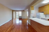 Located at 16-70 Bell Blvd in the Bayside neighborhood of Queens, New York, this single-floor residential unit offers a functional and well-maintained layout. Rich hardwood flooring runs throughout the space, providing warmth and continuity across all rooms.

The living area is generously proportioned, featuring a sliding glass door that invites natural light and opens to an outdoor view of the surrounding neighborhood. A wall-mounted HVAC unit ensures year-round climate comfort. The space flows directly into the kitchen, which is designed in a galley style with warm oak cabinetry extending to the ceiling for ample storage, a gas range, microwave, and full-size refrigerator — all finished in white.

The bedrooms are well-sized, with one featuring dual windows that frame views of the Bayside skyline and neighboring buildings, and another offering a closet with bifold doors. Each bedroom includes its own wall HVAC unit. The bathroom is finished with white ceramic tile wainscoting, dark floor tiles, an oak vanity with a mirrored medicine cabinet, and classic chrome fixtures, creating a clean and practical space.

Overall, the unit presents a straightforward, livable layout with consistent finishes, solid natural light, and practical amenities throughout.