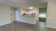 Located at 1000 Henrico Ln in Morrisville, NC, this single-floor residence offers a well-designed, open-concept living space that maximizes functionality and comfort. The interior is anchored by rich, dark hardwood-style flooring that extends seamlessly throughout the main living area, lending warmth and cohesion to the space.

The kitchen is a standout feature, outfitted with white shaker-style cabinetry, granite or stone-look countertops, and stainless steel appliances including a refrigerator and built-in microwave. A raised peninsula breakfast bar separates the kitchen from the main living area, providing a convenient space for casual dining or entertaining while maintaining an open, airy feel.

The layout is thoughtfully arranged, with clear sightlines connecting the kitchen, dining, and living zones. Neutral wall tones in soft beige create a versatile backdrop that complements a variety of interior styles. A built-in desk nook or secondary counter area is visible off to the side, offering a dedicated workspace or utility area. Standard white panel doors and clean white trim work throughout contribute to a crisp, tidy aesthetic. The overall ambiance is practical and move-in ready, suited for everyday living in a well-maintained residential setting.