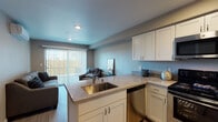 Located at 2401 Broadway St in Vallejo, California, this single-floor residence offers a thoughtfully designed layout with modern finishes throughout. The open-concept kitchen and living area serves as the heart of the home, where white shaker-style cabinetry, light stone countertops, and a peninsula with a stainless steel sink create a functional and visually cohesive space. Stainless steel appliances — including a range, microwave, and dishwasher — complete the well-equipped kitchen. Light wood-style flooring flows through the main living areas, enhancing the bright and airy atmosphere. The living room features a sliding glass door fitted with vertical blinds, opening to an outdoor balcony that brings in natural light and provides outdoor access. Two carpeted bedrooms offer comfortable retreats, each with neutral tones and recessed or ceiling lighting. The primary bedroom includes a closet, while both rooms provide ample space for furnishings. The bathroom is finished with wood-look flooring and features a glass-door walk-in shower, a toilet, and grab bar accessibility. Throughout the residence, a consistent neutral color palette of soft grays and warm taupes creates a calm, modern ambiance well-suited to everyday living.