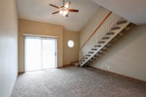 This two-floor home is designed with a practical and comfortable layout, offering well-proportioned spaces throughout. The main level centers around a spacious living area with vaulted ceilings, a ceiling fan, and a sliding glass door that opens to an outdoor space, filling the room with natural light. An octagonal accent window adds a distinctive architectural touch alongside the staircase, which features a wood handrail and white balusters leading to the upper level.

The kitchen is efficiently laid out with warm-toned wood cabinetry, granite-style countertops, a tile backsplash, and stainless steel appliances including a refrigerator and electric range. Stone-look tile flooring runs throughout the kitchen. An additional kitchenette area with matching cabinetry, countertops, and a utility sink provides extra functionality.

The bedrooms are carpeted and finished with neutral-toned walls, wood baseboards, and blinds-covered windows that allow natural light while maintaining privacy. Ceiling fans are present in multiple rooms. The bathrooms feature stone-look tile flooring, wood vanity cabinets with granite countertops, and a tub-shower combination, offering clean and functional finishes throughout.