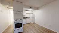 Located at 3230 E Roosevelt St in Phoenix, AZ, this efficient single-floor unit is thoughtfully designed to maximize every square foot. The layout includes a living area, kitchen, bathroom, and hallway, all unified by warm wood-look flooring that runs continuously throughout the space.

The living area is bright and open, featuring neutral beige walls, a textured ceiling, and a front entry door flanked by a sidelight window fitted with vertical blinds that allow natural light to filter in. Clean white baseboards and multiple electrical outlets make the space flexible for various arrangements.

The kitchen is well-appointed with white shaker-style cabinetry offering ample upper and lower storage, dark speckled countertops, a double-basin stainless steel sink, and white appliances including an electric range with overhead ventilation, a dishwasher, and a full-size refrigerator. A ventilation duct and overhead ceiling light keep the kitchen functional and practical.

The bathroom features a walk-in shower with white tile surround, a toilet, and a vanity with dark speckled countertop and undermount sink, complemented by the same wood-look flooring as the rest of the unit.

Overall, the space presents a clean, move-in-ready aesthetic with a consistent neutral palette, making it a practical and functional option in the Phoenix area.