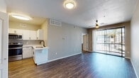 This single-floor residence offers a thoughtfully designed open-concept layout that seamlessly connects the kitchen and living areas. The kitchen is outfitted with white shaker cabinets accented by matte black hardware, a gray subway tile backsplash, quartz countertops, stainless steel appliances including a refrigerator, electric range, and microwave, and a deep single-basin sink with a black gooseneck faucet. Rich, dark hardwood-style flooring extends throughout the main living areas, adding warmth and visual continuity. The spacious living area benefits from natural light streaming through sliding glass doors fitted with vertical blinds, leading to an outdoor access point. A ceiling fan provides additional comfort. The bedrooms feature plush wall-to-wall carpeting, neutral gray walls, ceiling fans, and vertical blind-covered windows that allow ample natural light. One bedroom includes a mirrored closet door and access to a walk-in closet. The bathroom is clean and functional, featuring a dual-sink white vanity with matte black hardware, a full tub-shower combination, and wood-look tile flooring. A dedicated in-unit laundry closet with a full-size washer and dryer adds everyday convenience. The textured ceilings and consistent neutral palette throughout create a cohesive, move-in-ready atmosphere.