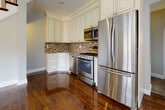 Located at 35-09 191st Street in Flushing, NY, this three-floor home blends classic architectural details with modern finishes throughout. The main level immediately impresses with richly stained hardwood floors that flow seamlessly through the space, complemented by a stunning coffered ceiling with recessed lighting and a handsome staircase featuring a dark wood banister and white balusters. Large multi-pane windows flood the living areas with natural light, creating a bright and welcoming ambiance. The kitchen is well-appointed with cream cabinetry extending to the ceiling, a decorative mosaic tile backsplash, granite countertops, and a full suite of stainless steel appliances including a gas range, built-in microwave, dishwasher, and French door refrigerator. Upper-level bedrooms showcase the same gleaming hardwood floors, crown molding, and generous closet space, with a full bathroom featuring stone tile flooring, a soaking tub with tiled surround, and a pedestal sink. A secondary bathroom offers warm wood cabinetry and a stone-topped vanity. The finished basement provides versatile additional living space with tile flooring, baseboard heating, and staircase access, making it ideal for a variety of uses.