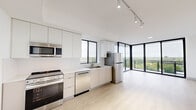 Located at 1155 NE 127th St in North Miami, FL, this contemporary 2-bedroom, 2-bathroom residence offers a well-designed layout with modern finishes throughout. Light hardwood flooring runs seamlessly across the living areas and bedrooms, complementing the clean, minimalist aesthetic of the space.

The open-concept kitchen is outfitted with flat-front cabinetry in white and warm neutral tones, white quartz countertops, and a full suite of stainless steel appliances including a range, dishwasher, microwave, and refrigerator. Large black-framed windows above the sink bring in natural light and frame lush treetop views. The kitchen flows directly into the living area, which is anchored by dramatic floor-to-ceiling glass walls that open to a private balcony with open-air views of the surrounding community.

Both bedrooms are bright and airy, each benefiting from expansive windows with verdant canopy views. The two bathrooms are identically finished with large-format neutral tiles, frameless glass-enclosed walk-in showers with rainfall fixtures, wood-toned floating vanities, white countertops, and illuminated mirrors. Each bedroom is paired with a dedicated closet. The unit also includes an in-unit laundry area, completing a thoughtfully arranged and functional floor plan.