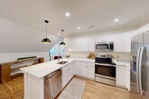 Located at 1 Pleasant St, Unit 307 in Cohasset, MA, this two-bedroom, one-bathroom unit offers a well-designed layout with a coastal-inspired aesthetic and quality finishes throughout. Warm hardwood floors flow seamlessly across the entire space, complementing the crisp white walls and trim that create a bright, airy atmosphere.

The open-concept kitchen and living area serves as the heart of the unit. The kitchen is outfitted with white shaker-style cabinetry, stainless steel appliances, quartz countertops, and a large waterfall island with a brass-toned sink and pendant lighting above — ideal for both cooking and casual dining. The adjoining living area features recessed lighting, a window offering tree-lined views, and a comfortable, welcoming ambiance.

The primary bedroom is a well-proportioned retreat with natural light streaming through a double-paned window and a closet. The second bedroom features a vaulted roofline with a charming angled ceiling, a window with greenery views, and a built-in nook. The full bathroom is finished in clean white tile with a soaking tub, a white vanity, and a window that brings in natural light. Throughout the unit, the architectural details — from the vaulted ceilings to the refined trim work — reflect a thoughtfully designed and move-in-ready space.