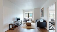 Located in Berkeley, CA, this single-floor residence offers a clean, contemporary design with warm wood-style flooring running throughout each room. The open living area is bright and welcoming, featuring a large window that allows natural light to fill the space while offering views of the surrounding neighborhood. The living room comfortably accommodates a seating arrangement and entertainment setup, making it well-suited for both relaxing and socializing.

The kitchen is outfitted with warm honey-toned cabinetry, dark granite countertops, and white appliances including a refrigerator, electric range, microwave, and dishwasher — providing a fully functional cooking space.

The bedrooms are generously sized with neutral white walls and large windows that invite natural light. Each room includes dedicated workspace with desks and chairs, making them practical for study or remote work. Closets with wire shelving systems provide ample organized storage.

The bathrooms are finished with clean, functional fixtures. One features a glass-enclosed shower/tub combination, while the other offers a standalone glass-door shower stall, both appointed with chrome hardware. The overall aesthetic throughout the residence is modern and understated, creating a comfortable and practical living environment.