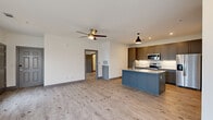 This well-appointed 2-bedroom, 1-bathroom residence offers a thoughtfully designed single-floor layout that maximizes both functionality and style. The open-concept living area is anchored by light wood-style flooring that flows seamlessly throughout, complemented by crisp white walls and ceiling fans in the main living spaces. Multiple large windows flood the living area with natural light and provide pleasant outdoor views.

The kitchen is a standout feature, showcasing a striking blue island with granite countertops, dark gray shaker-style cabinetry extending to the ceiling, a decorative hexagonal tile backsplash, and a full suite of stainless steel appliances including a side-by-side refrigerator, electric range, and over-the-range microwave. A pendant light above the island adds a modern finishing touch.

The spacious primary bedroom includes a ceiling fan, two windows with natural light, and direct access to a walk-in closet. The full bathroom features a gray shaker vanity with granite countertops, a large mirror, tiled tub-shower combination, and floating shelves for additional storage. The second bedroom also benefits from generous closet space. Throughout the residence, gray six-panel doors, coordinated trim, and recessed lighting contribute to a cohesive, contemporary aesthetic.