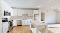 Located at 201 Eldorado Dr in Jordan, MN, this well-appointed 2-bedroom, 2-bathroom unit offers a clean, modern aesthetic with warm wood-look flooring and crisp white walls throughout. The open-concept kitchen and living area serves as the heart of the home, showcasing white shaker-style cabinetry, a geometric chevron tile backsplash, stainless steel appliances including a refrigerator, range, microwave, and dishwasher, and a freestanding kitchen island with built-in shelving — ideal for additional prep space and storage. The bedrooms are bright and well-sized, with the primary bedroom offering a walk-in closet. Natural light flows into the bedrooms through large windows with outdoor views. The unit includes two full bathrooms: one featuring a soaking tub and the other a walk-in shower, both finished with light flooring and clean white fixtures. Three closets and a dedicated utility room provide ample storage throughout. A private balcony extends the living space outdoors. Recessed lighting and a neutral color palette give the entire unit a fresh, contemporary feel.