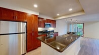 This two-floor residence combines modern finishes with an open, airy layout to create a comfortable and functional living environment. The kitchen is a standout feature, showcasing rich cherry wood cabinetry, dark granite countertops, a peninsula with a built-in sink, and a full suite of stainless steel appliances including a gas range, microwave, and refrigerator. Recessed lighting illuminates the space, which flows naturally into the adjoining dining and living areas.

The main living area impresses with soaring ceilings and a dramatic skylight that floods the room with natural light. Large floor-to-ceiling windows and sliding glass doors provide direct outdoor access and expansive views of the surrounding greenery. Light-toned hardwood floors run throughout, adding warmth and continuity. Track lighting accents the space with a modern, gallery-like quality.

The bedrooms offer plush carpeting and generous closet space. One bedroom features a striking arched window that frames outdoor views, while another provides a quiet, neutral retreat. The bathrooms are finished with large-format tile flooring, cherry wood vanities, and clean white fixtures, including a full tub-shower combination. A wet bar area with granite countertops and built-in cabinetry adds an additional layer of convenience and versatility to this well-rounded home.
