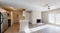 Located at 820 Canton Rd NE in Marietta, Georgia, this single-floor residence offers a thoughtfully designed open layout with a warm, neutral color palette and consistent wood-look flooring throughout the main living areas. The spacious living room serves as the centerpiece of the home, anchored by a classic white-mantled fireplace and bathed in natural light streaming through French doors that open to the outside. A ceiling fan adds comfort and function to the airy space. The kitchen is well-appointed with white shaker-style cabinetry, light countertops, a subway tile backsplash, a deep single-basin sink with a matte black faucet, and stainless steel appliances including a gas range and dishwasher. A peninsula with seating overhang connects the kitchen to the living area, enhancing the open-concept feel. An additional room adjacent to the kitchen offers flexible use as a dining area or secondary living space. The bedroom is generously sized, featuring plush carpet flooring, a ceiling fan, and multiple windows that invite natural light and views of the surrounding greenery. The bathroom is clean and modern, showcasing a wide white vanity with ample counter space, a vessel-style sink, white cabinetry with brushed metal hardware, and a large mirror with bright overhead lighting.