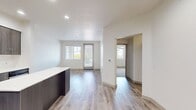 This 620 square foot apartment in Huntington Beach offers a blend of modern comfort and efficient living. The single-level layout comprises one bedroom, one bathroom, and an open-concept kitchen and living area. The primary bedroom, measuring 140 square feet, provides ample space and features a large window that allows natural light to flood in, creating a bright and airy atmosphere.

The kitchen is a standout feature, boasting sleek gray cabinetry, stainless steel appliances, and a practical island that doubles as a breakfast bar. White quartz countertops contrast beautifully with the dark cabinets, while recessed lighting enhances the modern aesthetic. The open layout seamlessly connects the kitchen to the living area, ideal for entertaining or everyday living.

The bathroom is generously sized and well-appointed, featuring a glass-enclosed shower, modern fixtures, and a large mirror. Light-colored tiles on the floor and walls contribute to a clean, spa-like feel. Throughout the apartment, you'll find a harmonious mix of materials, including plush carpeting in the bedroom and hallway, and durable wood-look flooring in the main living areas and kitchen.

Large windows in the living room and bedroom not only provide natural light but also offer views of the surrounding area, including glimpses of palm trees that hint at the apartment's desirable coastal location. The neutral color palette, predominantly whites and light grays, creates a canvas for personal styling while maintaining a fresh, contemporary ambiance.