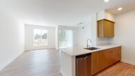 This single-floor residence features a clean, contemporary design with a cohesive aesthetic carried throughout each room. The open-concept layout connects the kitchen and living area seamlessly, creating a bright and functional shared space. Light wood-toned luxury vinyl plank flooring runs throughout the unit, complementing the crisp white walls and contributing to an airy, modern ambiance.

The kitchen serves as a central hub, anchored by a peninsula island with a quartz countertop and an undermount stainless steel sink. Warm wood-grain cabinetry provides ample storage, while stainless steel appliances—including a gas range, over-the-range microwave, refrigerator, and dishwasher—complete the well-equipped space. Recessed lighting and track lighting add both function and style.

The living area benefits from generous natural light through large windows and sliding glass doors fitted with vertical blinds, offering outdoor access. The bedroom is spacious and features a walk-in closet with built-in shelving, providing practical storage solutions.

Two bathrooms serve the unit: one features a tub-shower combination with white subway tile surround, and the other is a three-quarter bath. Both include wood-toned vanities with quartz countertops and large mirrors, maintaining the unit's consistent modern aesthetic.