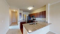 This single-floor residence offers a thoughtfully designed open-concept layout that seamlessly connects the kitchen and living areas. The kitchen is a standout feature, equipped with rich dark-wood cabinetry, granite countertops, a dual-basin undermount sink set within a central island, and a full suite of stainless steel appliances including a refrigerator, electric range, and microwave. Hardwood flooring anchors the kitchen, while plush carpet extends through the living areas and bedrooms.

The spacious living room is bathed in natural light from a set of large French doors that open to a private balcony, complemented by a ceiling fan and elegant crown molding. A wide hallway with flush-mount lighting connects the living spaces to the private quarters. Bedrooms are generously sized, each benefiting from multiple windows with outdoor views and ceiling fans.

The bathroom features granite-topped vanity cabinetry, a full soaking tub with white tile surround, and hardwood flooring. A walk-in closet with built-in shelving provides ample storage. An in-unit laundry area with washer hookups and overhead shelving adds everyday convenience. Throughout, warm neutral tones and crown molding details contribute to a cohesive and comfortable ambiance.