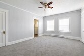 This well-laid-out 1-bedroom, 1-bathroom unit in Twin Falls, Idaho, offers a comfortable and functional living experience across a single floor. The entrance welcomes you into a generously sized living room, finished with soft carpet flooring, crown molding, and a ceiling fan with light fixture. Multiple windows dressed with blinds fill the space with natural light, while a baseboard heater ensures warmth year-round. The spacious bedroom continues the same warm, carpeted aesthetic, featuring crown molding, ceiling fan, and two bright windows that invite plenty of natural light. A closet door adds practical storage directly within the room, complemented by two additional closets throughout the unit. The kitchen is a standout, showcasing rich natural wood cabinetry, dark granite-style countertops, a stainless steel sink, and wood-look vinyl plank flooring. It is equipped with a white electric range and ample upper and lower cabinet storage for all kitchen essentials. The bathroom is clean and functional, offering a tub-shower combination with white surround, a mirrored medicine cabinet, and a shelf. Throughout, soft gray walls, white trim, and classic paneled doors lend a cohesive, tidy character to the entire unit.