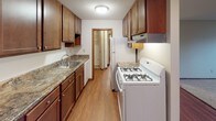 This single-floor residential unit offers a practical and comfortable layout with well-defined living spaces. The open living and dining area features warm hardwood-style flooring that flows toward the kitchen, creating a cohesive and inviting atmosphere. A ceiling fan overhead adds both style and function. Large windows throughout the unit allow for generous natural light and views of the surrounding outdoor environment, with baseboard heating units positioned beneath to ensure year-round comfort.

The galley-style kitchen is efficiently designed with rich, dark wood cabinetry lining both walls, granite-look countertops, and a full suite of white appliances including a gas range and refrigerator. Ample upper and lower cabinet storage makes the most of the space, while wood-look flooring ties the kitchen to the main living area.

The bedrooms are carpeted for comfort and each feature ceiling fans with light fixtures and sliding windows that bring in natural light. The unit includes a full bathroom finished with warm wood-toned cabinetry, a combined tub and shower with white tile surround, classic basketweave tile flooring, and a well-lit vanity mirror. A wall-mounted medicine cabinet provides additional storage. The overall aesthetic is clean, functional, and move-in ready.