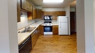 Located at 3510 W 53rd St in Sioux Falls, South Dakota, this single-floor unit offers a straightforward and functional layout across several distinct areas. The kitchen is equipped with warm oak cabinetry providing ample storage, a double-basin sink, electric range, built-in microwave, and a full-size refrigerator. Wood-look flooring runs throughout the kitchen, and a skylight-style ceiling fixture adds overhead illumination. A pass-through opening connects the kitchen to the adjacent living area, which is finished with neutral wall-to-wall carpeting and a textured ceiling. Two windows allow natural light into the living space, offering views of the surrounding exterior. The bedroom features the same carpeted flooring, a textured ceiling, and a double bifold closet with a built-in rod for storage. A window provides additional natural light. The bathroom includes a full-size soaking tub with an overhead shower, a curtain rod, a wall-mounted towel bar, and wood-look flooring that complements the neutral wall tones. Throughout the unit, consistent neutral finishes, textured ceilings, and practical fixtures create a cohesive and functional living environment.