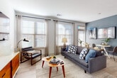 This single-story residence offers a thoughtfully designed open floor plan with a cohesive contemporary aesthetic. The living area is bright and inviting, featuring large windows with horizontal blinds and sheer curtains that allow generous natural light to fill the space. Light-toned hardwood-style flooring runs throughout the main areas, complementing neutral walls accented by a signature blue-gray feature wall. A private entry door with a transom window adds an architectural touch, while a dedicated dining nook provides a functional yet stylish space for everyday living.

The kitchen is well-equipped with granite countertops, gray shaker-style cabinetry, a classic white subway tile backsplash, and a full suite of stainless steel appliances including a range, microwave, and dishwasher. A connecting hallway leads to the private quarters, where two bedrooms offer comfortable retreats, each with natural light and carpeted flooring. The primary bedroom features a walk-in closet with wire shelving for organized storage. The full bathroom includes a granite vanity and a tub-shower combination. A dedicated laundry area houses a full-size washer and dryer, completing this practical and polished residence.