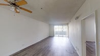 Located at 11657 Oxnard St in North Hollywood, Los Angeles, this single-floor unit offers a clean, functional layout with consistent hardwood-style flooring running throughout every room. The spacious living area is a standout feature, bathed in natural light from a full-width sliding glass door that opens to an outdoor area. A ceiling fan with wooden beam accents and a textured ceiling add character to the space. The open sightlines from the living area extend toward the kitchen pass-through, creating a connected and airy feel. The galley-style kitchen is efficiently designed with white cabinetry, granite-style countertops, a double basin sink, a gas range, a refrigerator, and a tile backsplash accent. The bedroom features mirrored sliding closet doors and neutral white walls, providing a calm and versatile space. Two full bathrooms are present, each with a tub-shower combination, granite-style vanity countertops, wood-look tile surround, and hardwood-style flooring. One bathroom includes a window for added natural light. Crisp white walls throughout the unit create a bright, neutral canvas. The overall ambiance is clean and move-in ready, suited for comfortable everyday living in a well-connected Los Angeles neighborhood.