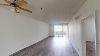 Located at 11657 Oxnard St in North Hollywood, Los Angeles, this single-floor unit offers a clean, functional layout with consistent hardwood-style flooring running throughout every room. The spacious living area is a standout feature, bathed in natural light from a full-width sliding glass door that opens to an outdoor area. A ceiling fan with wooden beam accents and a textured ceiling add character to the space. The open sightlines from the living area extend toward the kitchen pass-through, creating a connected and airy feel. The galley-style kitchen is efficiently designed with white cabinetry, granite-style countertops, a double basin sink, a gas range, a refrigerator, and a tile backsplash accent. The bedroom features mirrored sliding closet doors and neutral white walls, providing a calm and versatile space. Two full bathrooms are present, each with a tub-shower combination, granite-style vanity countertops, wood-look tile surround, and hardwood-style flooring. One bathroom includes a window for added natural light. Crisp white walls throughout the unit create a bright, neutral canvas. The overall ambiance is clean and move-in ready, suited for comfortable everyday living in a well-connected Los Angeles neighborhood.