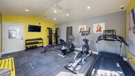 Located at 101 Chapel Ridge Dr in Union, Missouri, this fitness center offers a well-equipped exercise space designed to support a full range of workout routines. The room features vaulted ceilings with recessed lighting and a ceiling fan, creating an open, airy atmosphere despite its compact footprint. Large windows along multiple walls invite abundant natural light and provide views of the surrounding greenery, enhancing the overall workout environment.

The interior is finished with a bold two-tone color scheme of vibrant yellow and cool gray, paired with patterned carpet tile flooring accented with yellow striping — a cohesive design that energizes the space. A wall-mounted flat-screen television provides entertainment during workouts.

The facility is thoughtfully equipped with a variety of cardio machines, including treadmills, an elliptical, and a stationary bike. A multi-functional cable machine supports a wide range of strength training exercises, complemented by a dedicated free weight area featuring a tiered dumbbell rack. A flat workout bench and exercise mat provide space for floor-based training. A yellow bench offers convenient seating near the entrance. Motivational fitness artwork adorns the walls, adding a polished, purposeful aesthetic to this well-appointed community fitness center.