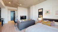 Located at 625 N 2nd Ave in downtown Phoenix, this contemporary studio showcases an open-concept layout that seamlessly integrates the living, dining, and kitchen areas into one cohesive space. The exposed concrete ceiling adds an industrial-chic character throughout, complemented by light wood-tone flooring that keeps the interior feeling bright and airy.

The kitchen is outfitted with dark cabinetry, white quartz countertops, a white tile backsplash, and a full suite of stainless steel appliances, including a refrigerator, dishwasher, and range. A matte black faucet and hardware provide a refined contrast to the clean, modern finishes.

The living and sleeping area benefit from a dramatic floor-to-ceiling window that floods the space with natural light and frames sweeping views of the Phoenix skyline and surrounding cityscape. Recessed lighting and white walls further enhance the sense of openness.

The bathroom features large-format tile flooring, a walk-in glass-enclosed shower, a floating wood vanity with a white countertop, and matte black fixtures that tie the design together cohesively. Additional conveniences include a dedicated closet and an in-unit laundry area, ensuring everyday functionality is well-addressed within this compact yet efficiently designed urban residence.