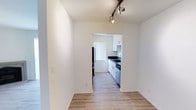This single-floor residence offers a clean, modern aesthetic defined by a bright and cohesive design throughout. The living and dining areas feature light hardwood-style flooring and crisp white walls, creating an open and airy atmosphere. Track lighting overhead adds both functional illumination and a contemporary design touch, allowing flexible lighting direction across the space.

The kitchen is accessible via an open passthrough and is thoughtfully designed with white shaker-style cabinetry, dark contrasting countertops, and stainless steel appliances, including a dishwasher and range. A black refrigerator anchors the entryway to the kitchen, while a window dressed with vertical blinds allows natural light to filter in, keeping the space bright and inviting. The cabinetry provides ample storage, and the layout is efficient, making good use of the available space.

The overall ambiance of the residence is fresh and minimalist, with a neutral color palette that lends itself well to a variety of décor styles. The seamless flow between the main living area and the kitchen enhances the sense of openness, making the space feel connected and functional. Clean lines and modern finishes throughout give this home a move-in-ready appeal.