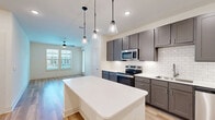 Located in Denton, TX, this well-appointed 2-bedroom, 2-bathroom residence offers a thoughtfully designed single-floor layout. The open-concept kitchen and living area serves as the heart of the home, anchored by a large white quartz island beneath three stylish pendant lights. The kitchen is outfitted with grey shaker-style cabinetry, a classic white subway tile backsplash, stainless steel appliances including a range, microwave, dishwasher, and refrigerator, and a stainless steel sink. The adjoining living room features a ceiling fan and large windows that flood the space with natural light and offer views of a pool area. Light hardwood-style flooring runs throughout the entire residence, providing a clean, cohesive aesthetic. Both bedrooms are bright and airy, each equipped with a ceiling fan and windows overlooking the outdoor pool. The primary bedroom connects to a dedicated closet with built-in shelving and hanging rods. Both bathrooms mirror each other in design, featuring dark cabinetry with white quartz countertops, undermount sinks, large mirrors, and tub-shower combos tiled in white subway tile. The overall ambiance is modern, clean, and move-in ready.