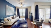 Located at Paddock Club in Fort Mill, South Carolina, this single-floor residence offers a thoughtfully designed layout that balances comfort and functionality. The entryway opens into a welcoming living room distinguished by rich hardwood-style flooring, a bold navy accent wall, and abundant natural light streaming through multiple windows dressed with floor-length drapes. A ceiling fan adds both style and practicality to the space.

The kitchen is outfitted with light maple cabinetry, granite-style countertops, a double basin sink, and black appliances including a range, microwave, and full-size refrigerator. The layout provides ample counter space and storage for everyday living.

The bedrooms are carpeted for comfort, each featuring ceiling fans and windows that invite natural light. The primary bedroom includes a generous dresser area, while the secondary bedroom showcases neutral tones and a large window with patterned drapes.

The bathroom features hardwood-style flooring, a wide vanity with a granite-style countertop, white cabinetry, and a tub-shower combination. A dedicated laundry area houses a full-size washer and dryer alongside wire shelving for additional storage. Throughout the residence, a cohesive navy and neutral palette creates a calm, polished atmosphere.