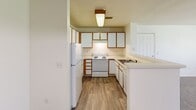 Located at 744 Mockingbird St in Brighton, Colorado, this single-floor unit offers a functional and accessible layout designed for comfortable everyday living. The open-concept design connects the kitchen and living area seamlessly, with a peninsula countertop serving as a natural divider between the two spaces. The kitchen is equipped with white cabinetry featuring wood-trim accents, a full suite of appliances including a refrigerator, electric range, and dishwasher, and is finished with durable wood-look flooring. A pendant light above the peninsula and flush-mount ceiling fixture provide ample illumination throughout. The spacious living area is carpeted and features a large window that invites natural light and outdoor views of the surrounding greenery, creating a bright and welcoming atmosphere. The bedroom continues the neutral color palette with soft carpeting and clean white walls, offering a quiet and versatile space. The bathroom is thoughtfully designed with accessibility in mind, featuring installed grab bars, a vanity with storage drawers, a large mirror, and wood-look flooring that ties cohesively to the rest of the unit. Throughout the space, the light neutral tones and clean finishes contribute to an open, airy ambiance well-suited for a variety of residents.