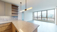 Located in Chicago's vibrant West Loop neighborhood, this high-rise residence at 164 N Peoria offers a sleek, contemporary design with an abundance of natural light. Floor-to-ceiling windows span multiple rooms, framing breathtaking panoramic views of the Chicago skyline, including the iconic Willis Tower, creating a striking visual backdrop throughout the space.

The open-concept living and dining area features light-toned hardwood-style flooring and a clean, minimalist aesthetic with crisp white walls. The kitchen is thoughtfully appointed with warm wood cabinetry, stone-look countertops, a full stone backsplash, and stainless steel appliances including a gas range and oven. A large kitchen island with pendant lighting ties the cooking and living spaces together seamlessly, while open shelving adds functional character.

The bedrooms continue the floor-to-ceiling window theme, each offering expansive skyline views and generous proportions. Two well-designed bathrooms complete the residence: one features a glass-enclosed walk-in shower with white tile surround and a wood-and-stone vanity, while the second offers a soaking tub with tiled surround and a matching wood vanity. Both bathrooms are finished with modern fixtures and frameless mirrors, maintaining the residence's cohesive, refined aesthetic throughout.