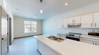 Located at 2971 N. Dr. Martin Luther King Jr. Dr in Milwaukee, WI, this thoughtfully designed one-bedroom, one-bathroom unit offers a clean, modern aesthetic throughout. The open-concept layout seamlessly connects the kitchen and living area, creating an efficient and welcoming flow. The kitchen is a standout feature, anchored by a central island with a double-basin sink and pendant lighting overhead. White cabinetry with sleek black hardware, light quartz-style countertops, and a full suite of stainless steel appliances — including a range, refrigerator, and microwave — complete the contemporary look. Light wood-tone flooring runs throughout the main living area, adding warmth to the bright, neutral color palette. The bedroom offers a comfortable and quiet retreat, carpeted for comfort, with a large multi-panel window that fills the room with natural light and provides views of the surrounding neighborhood. A dedicated closet adds practical storage. The bathroom features light wood-tone flooring, a walk-in shower with clean white surrounds, and a modern door with contemporary hardware. Recessed lighting and large windows ensure the space feels open and airy throughout.