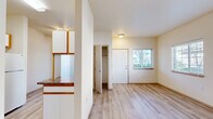 This thoughtfully laid-out one-bedroom, one-bathroom unit offers a comfortable and functional living space across a single floor. Light wood-tone laminate flooring runs consistently throughout, creating a cohesive and clean aesthetic from room to room.

The combined kitchen and living area forms the heart of the unit. The kitchen is well-equipped with white cabinetry featuring warm wood-tone trim, dark granite-style countertops, a double sink, an electric range, a ventilation hood, and a full-size refrigerator — providing ample storage and counter space for everyday cooking. The living area is open and bright, with neutral white walls and a wall-mounted heater unit.

The bedroom is a comfortable, well-proportioned room featuring two windows that invite natural light and outdoor views of surrounding greenery. A notable feature is the dual closets with built-in hanging rods, offering excellent storage capacity. The entry foyer area provides a dedicated transition space with an adjacent closet and a window beside the front door.

The bathroom includes a full-size soaking tub and shower combination, a vanity with matching dark countertop and white cabinetry, and a wall-mounted mirror. Light wood flooring continues into this space, maintaining the unit's consistent design language throughout.