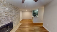 This single-floor residence offers a well-designed open-concept layout that seamlessly connects the living area to the kitchen. The living room serves as the focal point of the space, anchored by a full-height stacked-stone accent wall housing a fireplace, which adds both texture and warmth to the room. Wood-style flooring runs throughout the main living areas, complemented by a ceiling fan overhead. A sliding glass door with vertical blinds allows natural light to fill the room and provides access to the exterior.

The kitchen is positioned adjacent to the living area and features dark-toned cabinetry, white countertops, and stainless steel appliances including a range, microwave, and refrigerator. A pass-through counter connects the kitchen to the living space, enhancing the open feel. The kitchen also benefits from its own dedicated wood-style flooring and overhead lighting.

The bedroom is carpeted and receives natural light through a window with outdoor tree views. The bathroom includes a tiled tub-and-shower combination. A dedicated laundry room accommodates a full-size washer and dryer with wire shelving above, adding practical everyday convenience to the overall layout.
