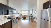 Located at 12850 SW Ash Ave in Tigard, Oregon, this one-bedroom, one-bathroom apartment offers a smart, efficient layout with modern finishes across a single floor. The kitchen is a standout feature, equipped with dark espresso cabinetry, stainless steel appliances including a range, microwave, and dishwasher, and clean white countertops. Light wood-style flooring runs throughout, lending warmth and visual continuity to the space. The entry flows directly into the kitchen, which opens toward the living area, creating a cohesive, open feel. The living room is bright and welcoming, with large windows that bring in generous natural light and offer views of the surrounding greenery. The bedroom is a comfortable retreat, featuring windows with outdoor views, warm neutral walls, and direct access to a closet and a conveniently placed in-unit stacked washer and dryer. The bathroom is clean and functional, appointed with a tub-shower combination, white fixtures, and a dark-toned vanity with a light countertop. Throughout the unit, the design emphasizes simplicity and functionality, with neutral tones and contemporary details that create a calm, livable atmosphere well-suited for everyday comfort in the heart of Tigard.