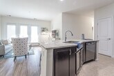 Located at 3000 Conservancy Drive in Chesapeake, Virginia, this single-floor residence offers a well-designed layout with a bright, open-concept living and dining area. The living room features wood-look flooring, crown molding, and a set of French doors with wide slatted blinds that invite abundant natural light and provide access to the outdoors. The kitchen is appointed with rich dark cabinetry, a tile backsplash, granite-topped peninsula with bar seating, and black appliances. A dedicated dining area sits adjacent to the kitchen, complete with pendant lighting and views into the living space. The primary bedroom is generously sized with plush carpeting, natural light from oversized windows, and access to an en suite bathroom featuring a dual-sink vanity with dark wood cabinetry and a separate walk-in shower with glass enclosure. A second bedroom also features carpet flooring, a large window, and a closet. A full secondary bathroom mirrors the clean, neutral finishes found throughout the home. Completing the layout is a dedicated in-unit laundry room equipped with a full-size washer and dryer. The home maintains a cohesive, neutral palette throughout, lending a clean and contemporary aesthetic.