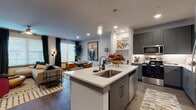 This single-story residence showcases a thoughtfully designed open-concept layout where the kitchen, dining, and living areas flow seamlessly together. The kitchen serves as a central hub, anchored by a large island with a white quartz countertop, an undermount sink, and seating for two. Sleek gray cabinetry lines the walls, complemented by stainless steel appliances, under-cabinet lighting, and two pendant lights that hang above the island. A built-in desk nook adjacent to the kitchen provides a dedicated workspace.

The living area is bright and welcoming, featuring wood-style flooring, a ceiling fan, and multiple windows dressed with blinds and dark curtains that allow for flexible light control. The dining area accommodates a round table and benefits from natural light through a large window. The bedroom continues the warm aesthetic, offering a generous window with outdoor views, wood-style flooring, and ample wall space. The full bathroom features gray tile surround, a soaking tub with shower, a wide vanity with dual sinks, and a large mirror. An in-unit laundry area completes this well-rounded, functional residence.