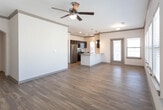 This single-story unit in Odessa, Texas, offers a well-designed layout with a consistent blend of modern finishes and functional living spaces. The open living area is a standout feature, showcasing warm hardwood-style flooring, neutral-toned walls, dark crown molding, and a row of large windows fitted with blinds that allow abundant natural light and outdoor views. Ceiling fans are present throughout, contributing to both comfort and airflow.

The kitchen is thoughtfully appointed with rich dark cabinetry, granite countertops, and stainless steel appliances including a refrigerator, microwave, and electric range. A central island with an undermount sink and pendant lighting above serves as a functional and stylish focal point, with direct sightlines to the living area.

The bedrooms offer plush carpeting, ceiling fans, and windows that bring in natural light. The primary bathroom features a double-sink granite vanity with dark cabinetry, a large mirror, hardwood-style flooring, and access to a walk-in closet with built-in shelving. A secondary bathroom includes a single vanity with granite countertop and a full tub-shower combination, maintaining the same cohesive design aesthetic found throughout the unit.
