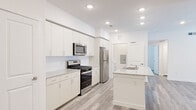 This single-floor unit showcases a clean, contemporary design throughout, unified by light wood-style vinyl plank flooring and crisp white walls. The open-concept kitchen is a standout feature, equipped with stainless steel appliances including a gas range, over-the-range microwave, and refrigerator. White shaker-style cabinetry extends to the ceiling, offering generous storage, while granite countertops complement the central island, which includes a sink and additional prep space. Recessed lighting illuminates the kitchen and flows into the adjoining living area, which benefits from natural light through large windows and features a ceiling fan.

Bedrooms are comfortably sized, each with ceiling fans and window blinds. One bedroom includes built-in shelving, ideal for a home office or storage needs. The bathroom is finished with marble-style tile flooring, a granite vanity, and a tub-shower combination with coordinating tile surround. A dedicated walk-in closet with wire shelving provides ample storage. The in-unit laundry area accommodates a full-sized washer and dryer and includes overhead wire shelving. The overall aesthetic is bright, functional, and move-in ready.