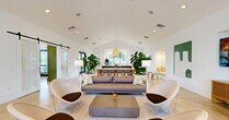 Located at 9145 Flying Eagle Dr in Fort Myers, Florida, this single-story clubhouse offers a well-appointed community gathering space defined by clean, contemporary design and an inviting Florida aesthetic. The single floor spans a generous footprint, encompassing multiple functional areas that flow seamlessly into one another.

The main lounge area anchors the space with soaring vaulted ceilings, polished concrete floors, and abundant natural light streaming through large picture windows. A built-in leather bench seat frames a striking pool-view window, complemented by terrazzo round tables and woven lounge chairs. Sliding barn doors with frosted glass panels provide flexible room division while maintaining an airy, open feel.

A central bar and counter area with bar seating serves as an informal gathering hub, flanked by lush tropical plants that reinforce the Florida surroundings. A flat-screen display and tasteful wall art add personality to the lounge.

Two dedicated private office spaces offer functional workstations, each benefiting from large windows, ample shelving, and vibrant, playful design accents including bold pendant lighting. A reception area near the main entrance features a sleek green-accented desk, tall custom cabinetry, and direct glass door access to the outdoors. Throughout, the consistent use of white walls, natural textures, and tropical greenery creates a bright, welcoming, and professional community environment.
