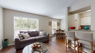 This two-bedroom, one-bathroom residence is thoughtfully laid out across a single floor, offering a comfortable and cohesive living experience. The open-concept living and dining area is anchored by rich hardwood-style flooring that runs throughout the main living spaces, creating a warm and inviting atmosphere. Large windows fitted with white blinds fill the room with natural light while framing views of lush greenery outside. A breakfast bar separates the living area from the galley-style kitchen, which features white cabinetry, granite-style countertops, a full suite of black appliances including a refrigerator, range, and built-in microwave, and ample storage on both sides of the corridor. The two bedrooms are carpeted for comfort and each include a ceiling fan for added convenience. The primary bedroom offers walk-in closet access adjacent to the shared full bathroom. The bathroom is appointed with a vanity featuring a single sink, white cabinetry, and a well-lit mirror above. Neutral wall tones throughout the residence lend a clean, versatile backdrop suited to a variety of décor styles. The overall layout is efficient and practical, making excellent use of the available space while maintaining a comfortable, residential ambiance.