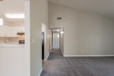This single-floor residence offers a thoughtfully designed layout that balances open communal spaces with comfortable private quarters. The living area is a standout, featuring soaring vaulted ceilings that lend a sense of grandeur and airiness. Plush carpet underfoot and a tile-surround fireplace create a warm, inviting atmosphere, while a sliding glass door opens to an outdoor area, flooding the room with natural light. A wide hallway connects the living space to the private areas of the home, maintaining an easy flow throughout.

The kitchen is well-appointed with white shaker-style cabinetry, marble-look countertops, and a breakfast bar that opens to the living area. Black appliances, including a refrigerator and range, provide a modern contrast, and dual pendant lights add a stylish finishing touch.

The bedrooms are carpeted and bathed in natural light through multiple windows with views of surrounding greenery. The primary bedroom connects to an en suite bathroom featuring wood-look flooring, a marble-top vanity, and a spacious walk-in closet with built-in shelving. A second bathroom mirrors the updated finishes, offering wood-look flooring and a similarly elegant vanity, ensuring a consistent and polished aesthetic throughout the home.