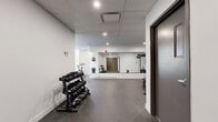 Located at 5480 Avenue Henri-Julien in the heart of Montréal, this fitness facility offers a clean, modern exercise space designed to support a full range of workout routines. The single-floor gym is finished with a durable speckled rubber floor, crisp white walls, and a suspended tile ceiling equipped with recessed pot lighting that ensures bright, even illumination throughout.

Large wall-mounted mirrors span multiple sides of the room, visually expanding the space and allowing users to monitor their form during exercise. The strength training area features a multi-functional cable machine and a dedicated adjustable weight bench, while a well-stocked dumbbell rack provides a comprehensive range of free weights for varied training needs. On the cardio side, the facility includes a treadmill and a stationary spin bike, positioned near a window that draws in natural light and offers a view of the surrounding urban streetscape.

Baseboard heating runs along the perimeter walls, ensuring year-round comfort, and an air conditioning unit provides climate control during warmer months. Access to the gym is through a set of dark-framed doors, lending a polished, contemporary finish to the entryway. The overall ambiance is functional and professional, making this gym a practical and well-appointed fitness amenity.