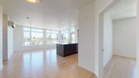 This single-floor residence showcases a clean, contemporary design throughout, with light hardwood flooring and crisp white walls creating a bright, cohesive aesthetic. The open-concept living and kitchen area serves as the heart of the space, where floor-to-ceiling windows and transom windows along multiple walls flood the interior with abundant natural light and frame expansive outdoor views of the surrounding neighborhood and skyline. The kitchen is outfitted with dark cabinetry, stainless steel appliances including a range, microwave, and refrigerator, and a large center island with a white countertop and integrated sink, offering generous workspace and casual seating potential.

The bedrooms continue the light hardwood flooring and feature large picture windows that draw in natural light and outdoor views. Each bedroom includes closet space, with at least one room offering a walk-in closet with built-in shelving. A wall-mounted mini-split system provides individual climate control. The bathrooms are finished with neutral tile work, including a glass-enclosed walk-in shower with subway tile surround and a separate tub with a handheld showerhead. Recessed lighting throughout reinforces the unit's modern, polished character.