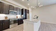 Located at 3711 S SH 161 Frontage Rd in Grand Prairie, TX, this thoughtfully designed one-bedroom, one-bathroom residence offers a well-organized single-floor layout with a seamless flow throughout. The open-concept kitchen and living area serves as the heart of the home, showcasing rich dark espresso cabinetry, a white subway tile backsplash, stainless steel appliances, and a granite-topped kitchen island with an undermount sink and matte black faucet. A modern angular chandelier adds a contemporary touch overhead, while light wood-look flooring runs throughout the main living areas, lending a clean and cohesive aesthetic. The living room is bright and airy, benefiting from a large window that invites natural light into the space. The bedroom is carpeted for comfort and features a window with blinds, providing a quiet and restful retreat. An adjacent walk-in closet offers ample built-in shelving and hanging space on both sides. The bathroom is elegantly appointed with a wide dark-wood double vanity, granite countertop, a large framed mirror, contemporary lighting, and a glass-enclosed shower. Light wood-look tile flooring completes the bathroom's refined look, tying together the unit's consistent modern design language.