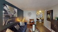 This single-floor residence offers a thoughtfully designed layout that balances comfort and contemporary style throughout. The living area serves as the focal point of the unit, featuring dark hardwood-style flooring, a bold accent wall in deep charcoal, and a large front-facing window that invites natural light. The space flows naturally into a dedicated dining area, distinguished by geometric wall art and a sleek round table with modern seating.

The galley-style kitchen is efficiently arranged with dark cabinetry, speckled grey countertops, a mosaic tile backsplash, and white appliances including a range and refrigerator. Track lighting overhead keeps the workspace well illuminated.

Two bedrooms provide comfortable accommodations, each equipped with ceiling fans and windows fitted with blinds. The primary bedroom features a deep teal accent wall and ample space for a king-sized bed, while the second bedroom maintains a neutral palette with dark hardwood-style flooring.

The bathroom includes a dark vanity with grey countertops, a mosaic tile backsplash, and framed mirror, creating a clean and modern aesthetic. Throughout the unit, consistent flooring, coordinated color tones, and curated décor details contribute to a cohesive and polished overall ambiance.